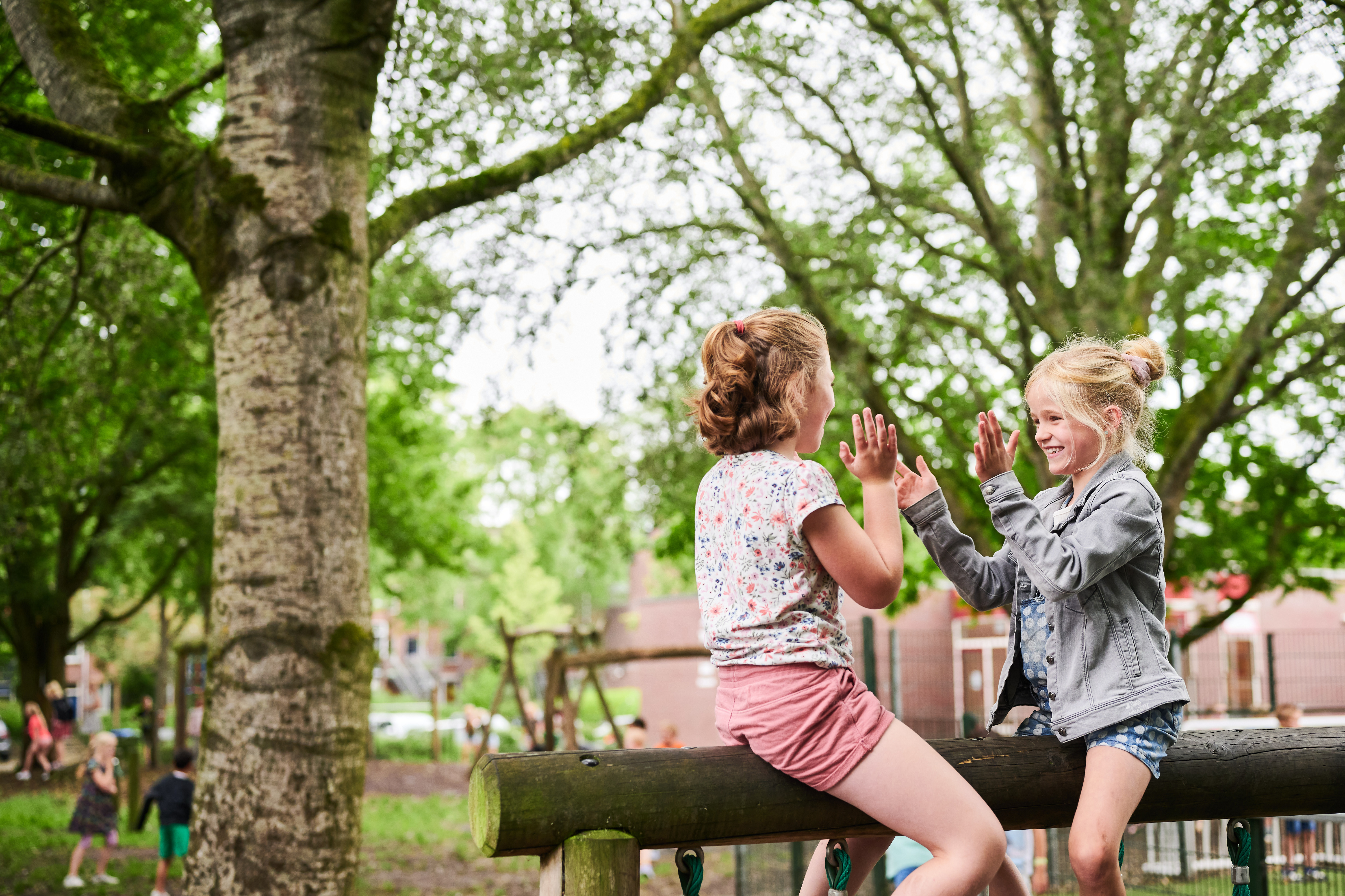 Twee leerlingen spelen buiten op houten balk.
