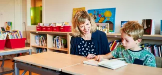 Leerkracht en leerling lezen samen in een boek.