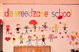 Een knutselwerk over de Vreedzame School hangt op school op de muur.