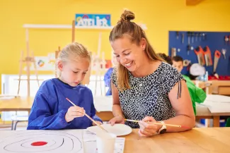 Leerling en juf schilderen samen in klaslokaal.